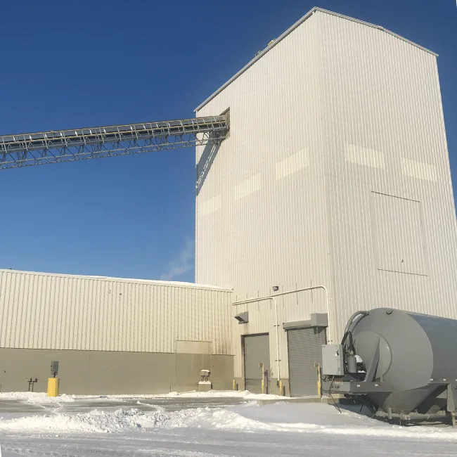 Industrial processing plant with an elevated conveyor bridge feeding a tall metal-clad tower