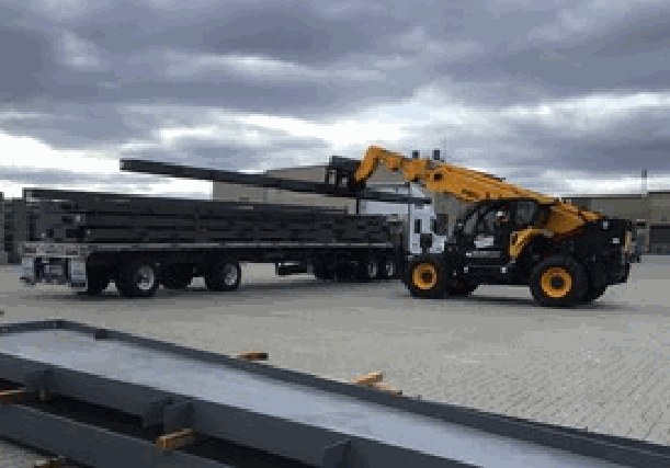 Steel beams loaded on a flatbed trailer beside a telehandler at a jobsite