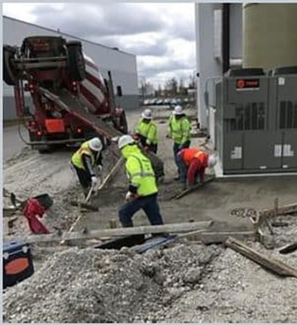 Crew placing concrete beside rooftop mechanical units at a commercial jobsite