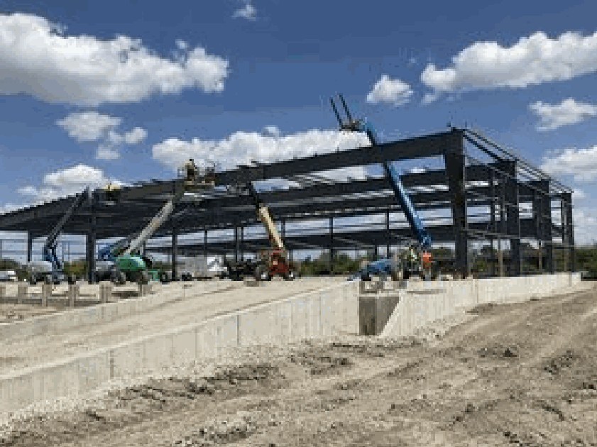 Steel frame of a pre-engineered metal building rising above a poured foundation