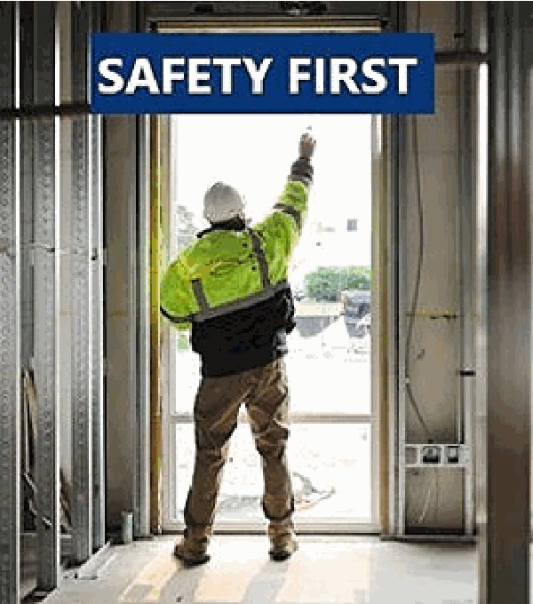 Worker in a high-visibility vest beneath a Safety First sign at a jobsite entrance