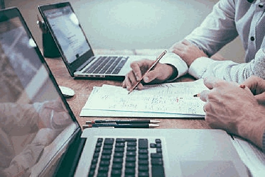 Two people working through project figures on a laptop and a notepad