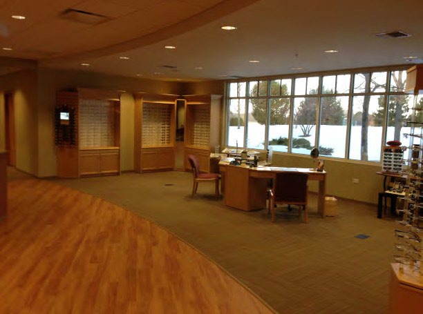 Eye centre interior with a reception desk, wood floor and eyewear display shelving in Huntley, Illinois